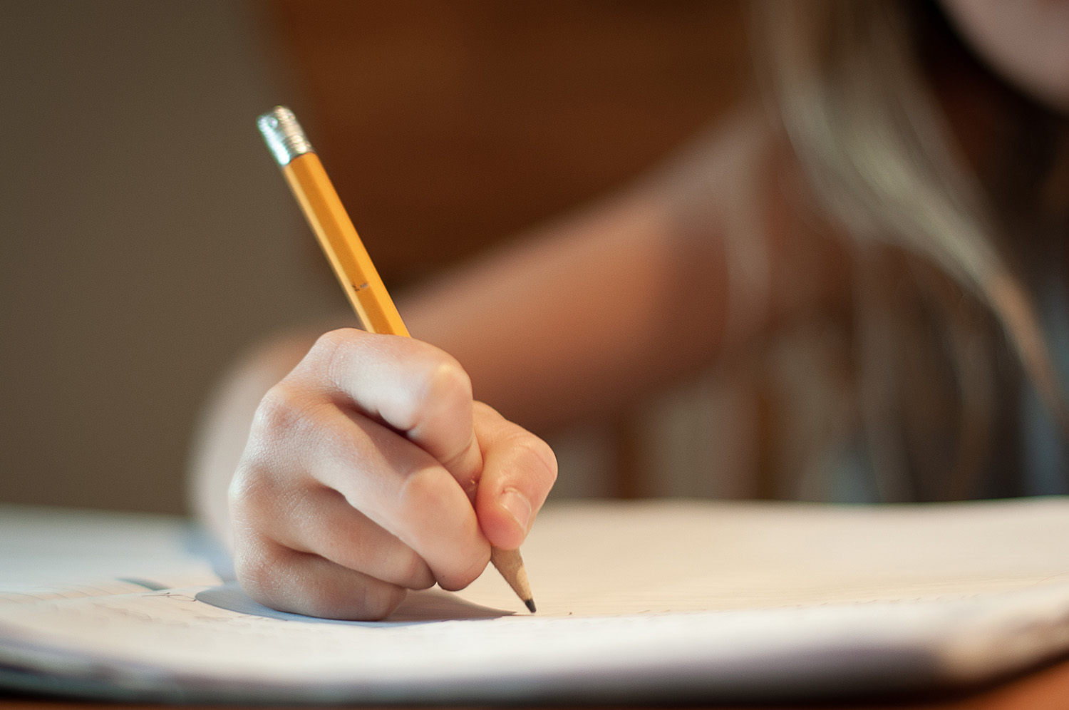 Närbild på en ung skolelevs hand som skriver med en blyertspenna på ett skrivblock